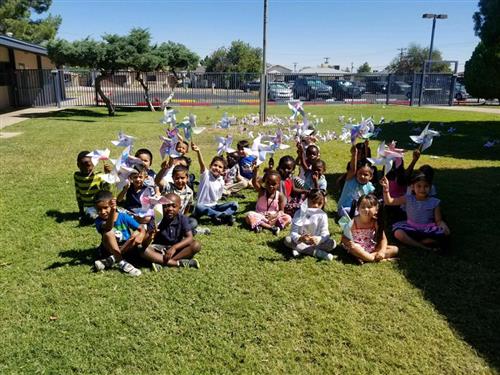 students holding paper pinwheels while sitting on the grass